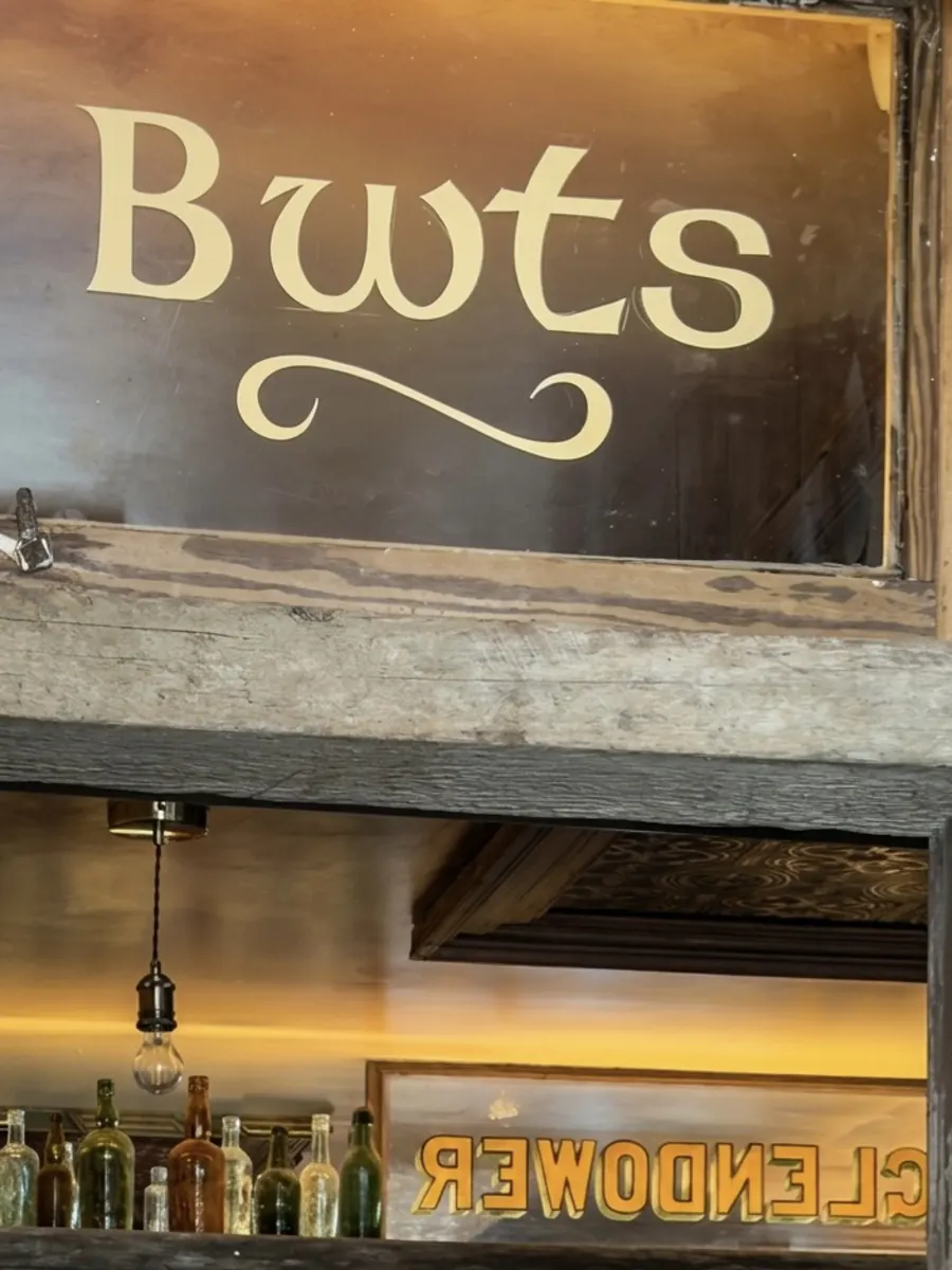 The gilded “Bwts” glass sign above the bar — Welsh for boots