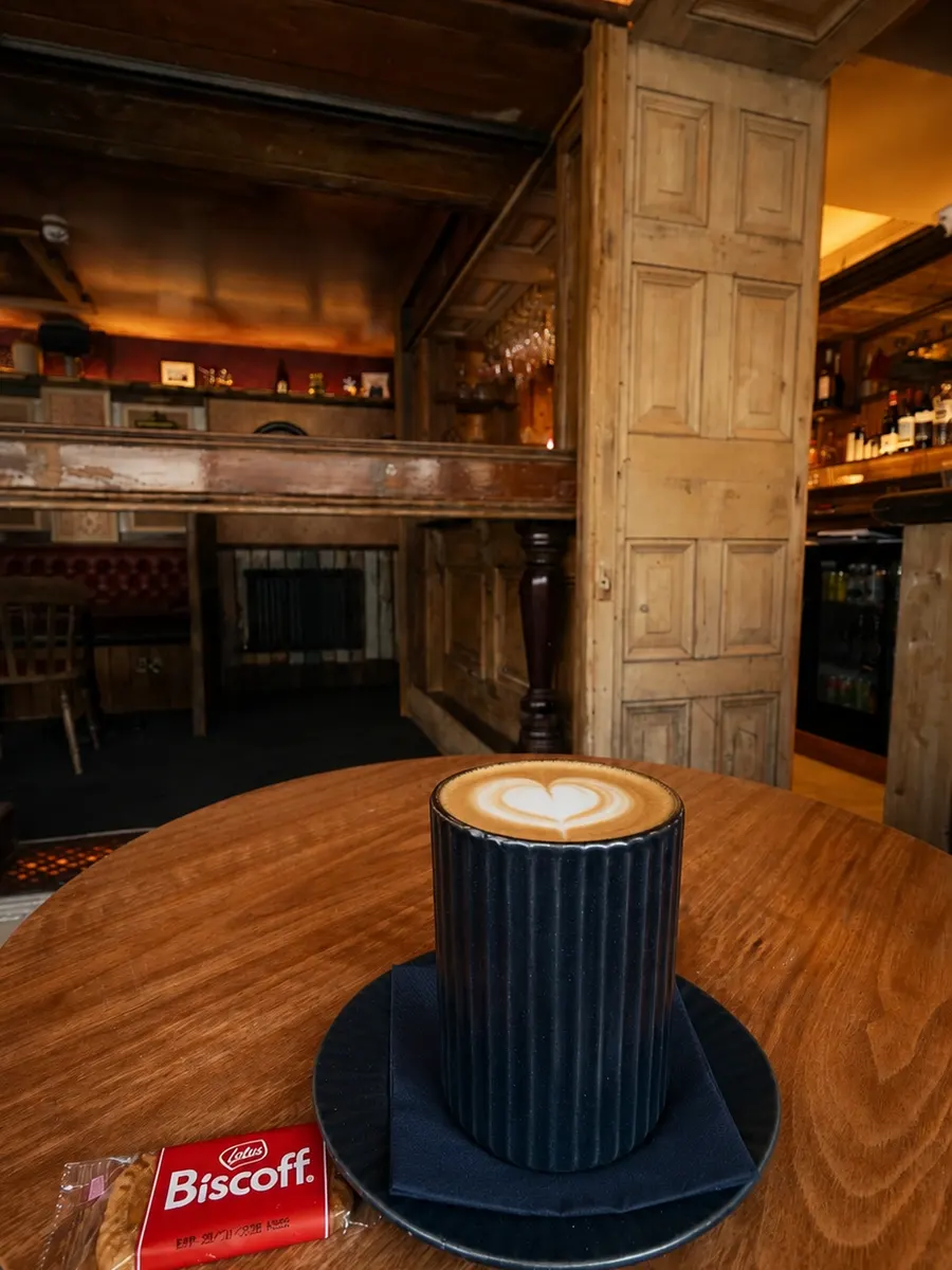 A flat white with latte art on a wooden table at Leicester House, Glynneath